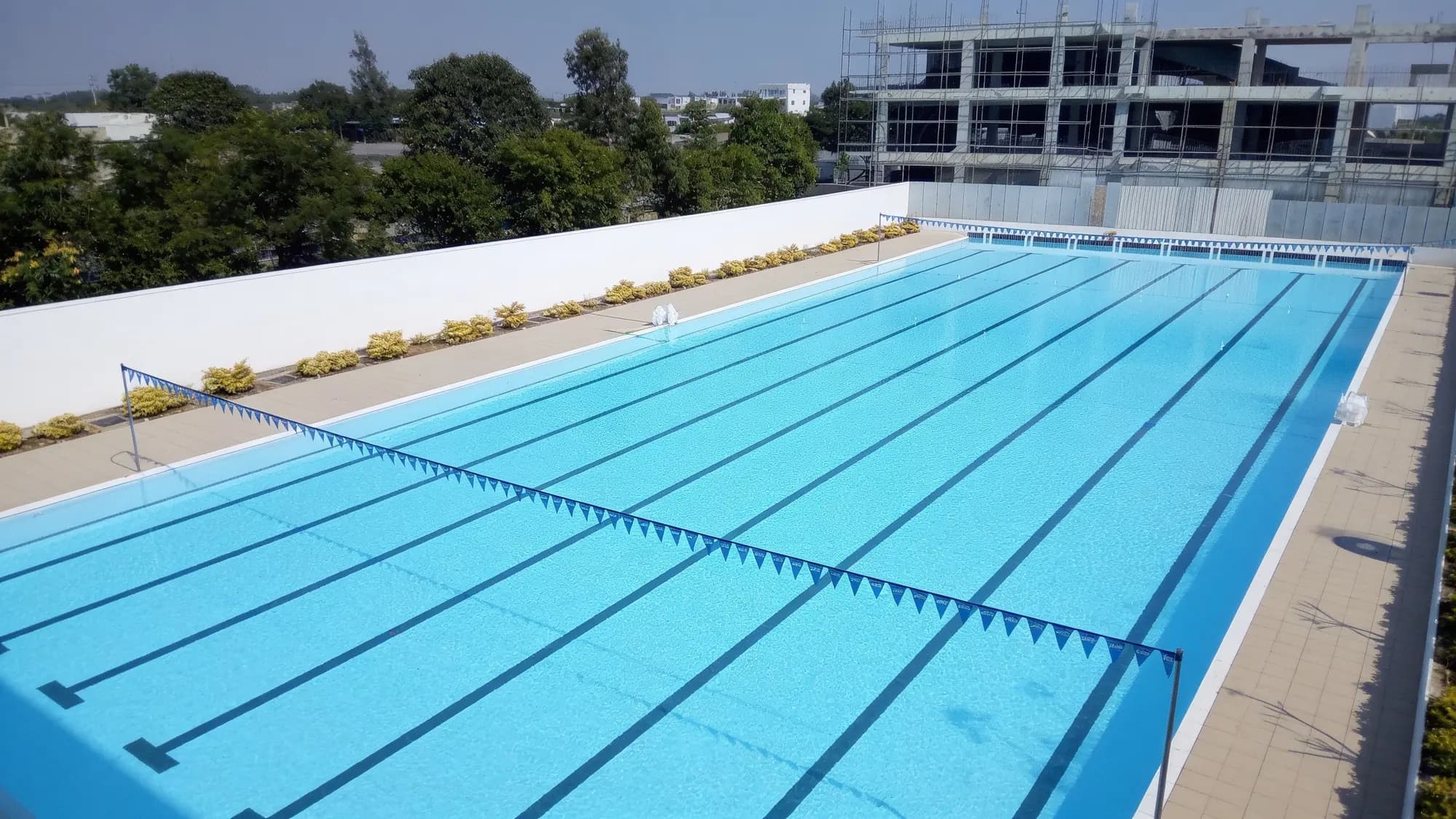 Aerial drone view of an Olympic-size competition swimming pool built by Oceanides, with lane markings and pennant flags.
